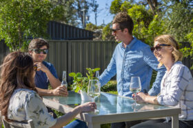Image of 4 people having a casual drink with a grey Colorbond fence in the background